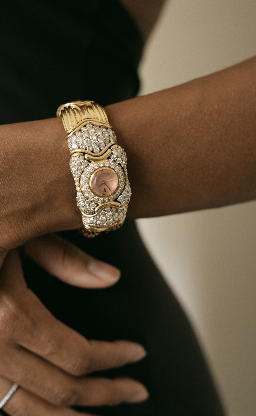 Hand wearing diamond-set gold watch on marble